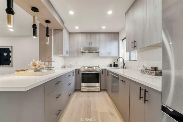 kitchen with appliances with stainless steel finishes, a sink, gray cabinets, a peninsula, and under cabinet range hood