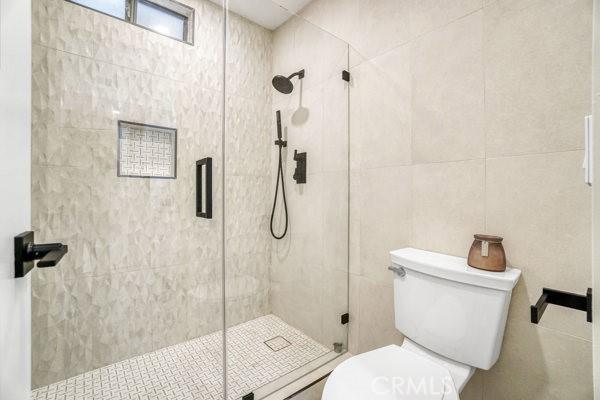 bathroom featuring toilet, tile walls, and a shower stall