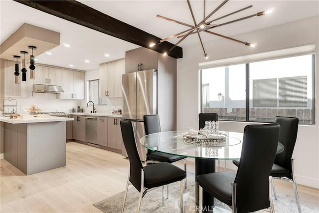 dining area with sink, light wood-type flooring, beamed ceiling, and a chandelier