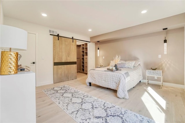 bedroom with baseboards, light wood-type flooring, a barn door, and visible vents