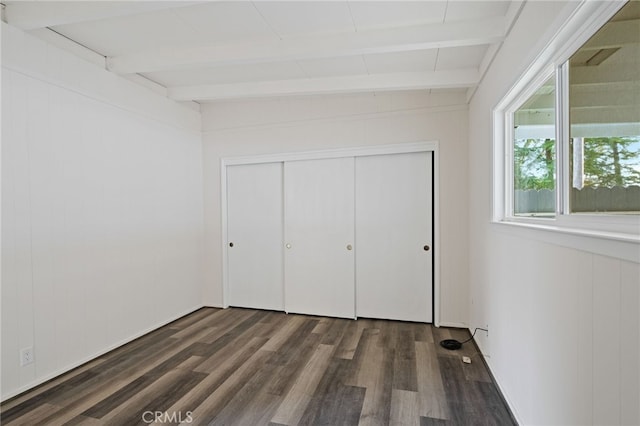 unfurnished bedroom with a closet, dark hardwood / wood-style flooring, and beam ceiling