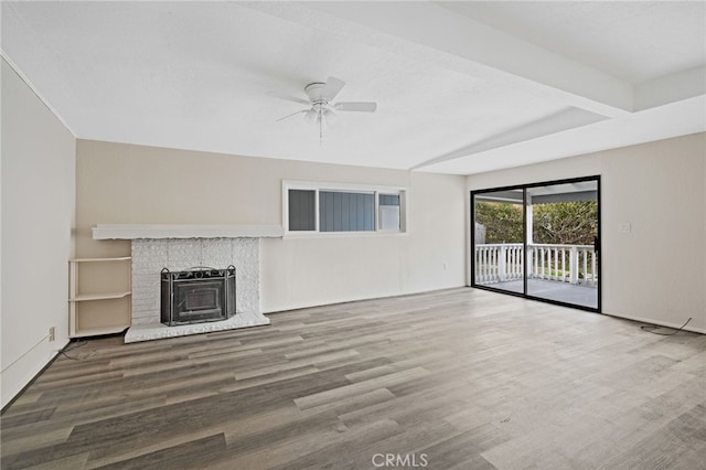 unfurnished living room featuring ceiling fan, hardwood / wood-style floors, beam ceiling, and a fireplace