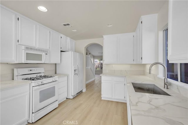 kitchen with light stone countertops, white appliances, white cabinets, light hardwood / wood-style floors, and sink