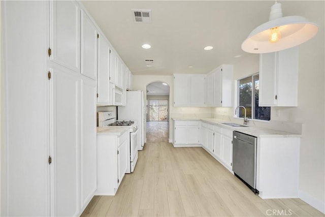 kitchen with white appliances, white cabinetry, sink, hanging light fixtures, and light wood-type flooring