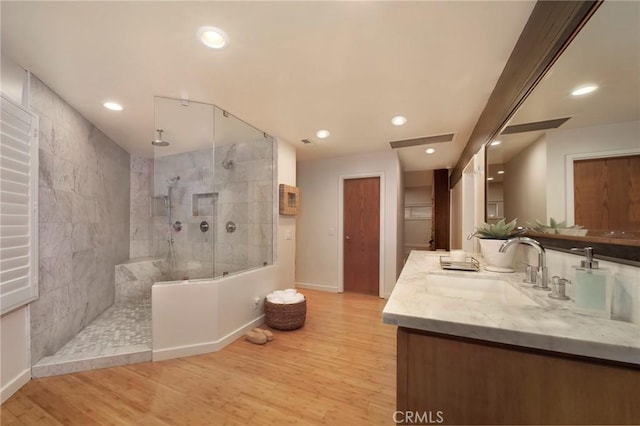 bathroom with tiled shower, vanity, and wood-type flooring