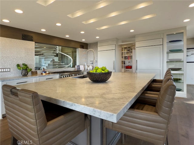 kitchen featuring a large island, sink, paneled built in refrigerator, white cabinets, and a kitchen bar