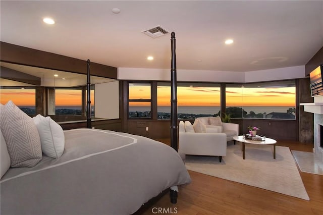 bedroom with a premium fireplace, a water view, and wood-type flooring