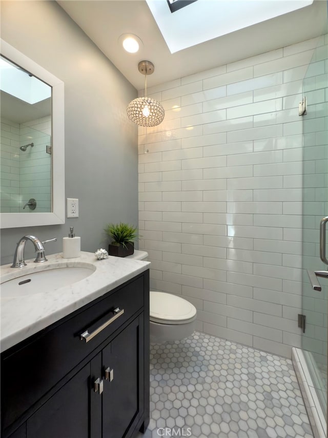 bathroom featuring toilet, a shower with shower door, a skylight, vanity, and tile patterned flooring