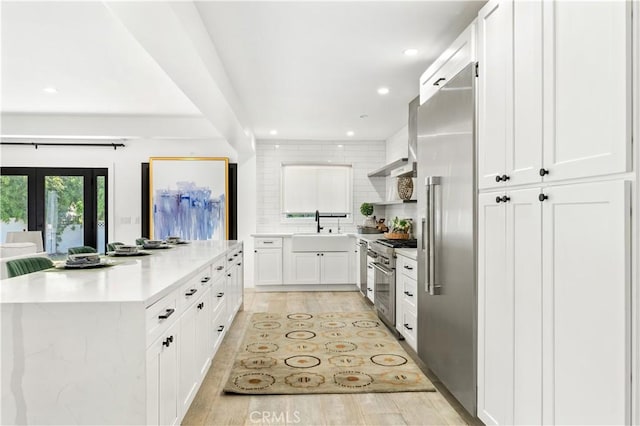 kitchen featuring white cabinetry, tasteful backsplash, light wood-type flooring, high end appliances, and sink