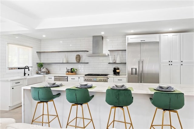 kitchen with tasteful backsplash, a kitchen island, a kitchen bar, appliances with stainless steel finishes, and wall chimney exhaust hood