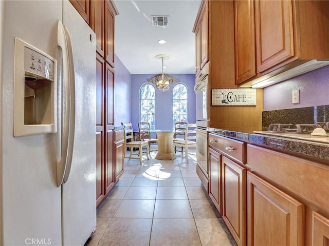 kitchen with stovetop, white refrigerator with ice dispenser, hanging light fixtures, a chandelier, and light tile patterned floors