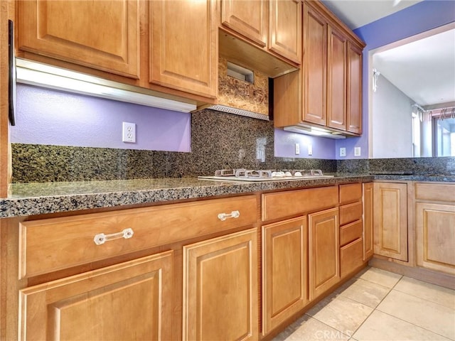 kitchen featuring backsplash, light tile patterned floors, white gas stovetop, and dark stone countertops