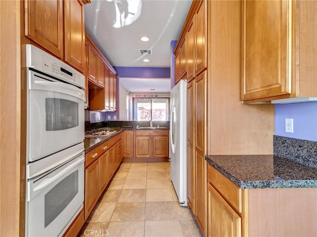 kitchen with white appliances, light tile patterned floors, and dark stone counters