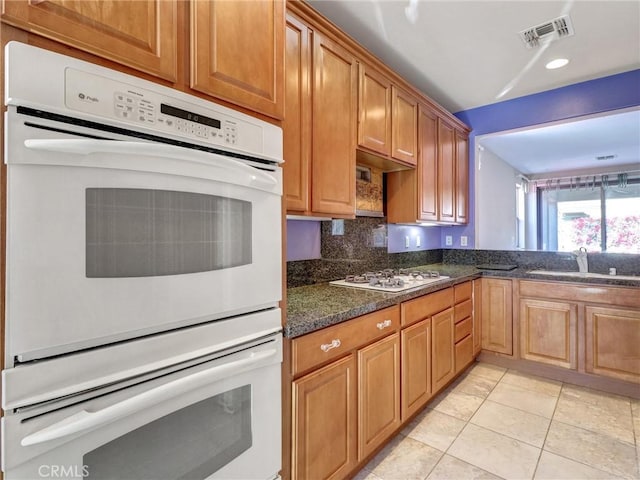 kitchen featuring white appliances, dark stone counters, decorative backsplash, sink, and light tile patterned flooring