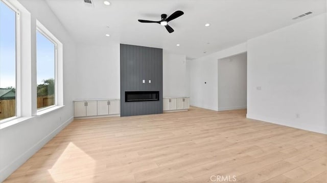 unfurnished living room with ceiling fan, a fireplace, and light wood-type flooring