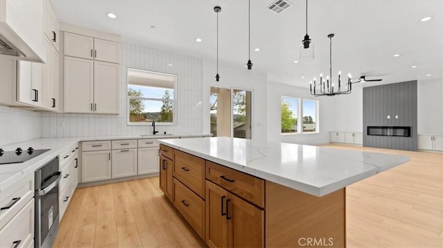 kitchen with a spacious island, white cabinetry, hanging light fixtures, light stone counters, and black electric cooktop