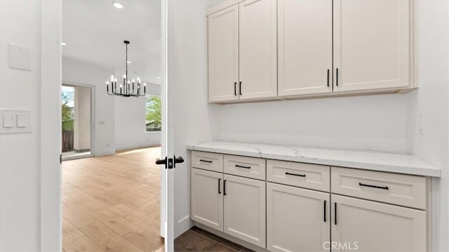 bar with light stone countertops, white cabinetry, and hanging light fixtures