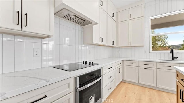 kitchen featuring black electric stovetop, stainless steel oven, custom range hood, white cabinets, and sink