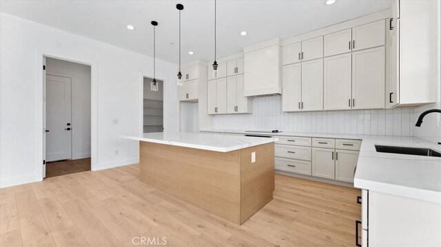 kitchen with premium range hood, pendant lighting, a kitchen island, sink, and white cabinets