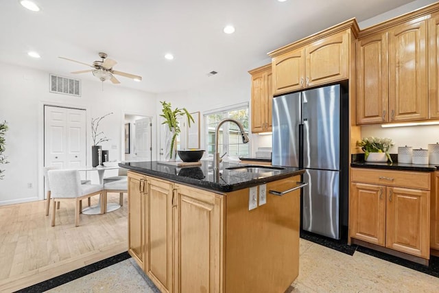 kitchen with a center island, dark stone counters, sink, ceiling fan, and stainless steel refrigerator