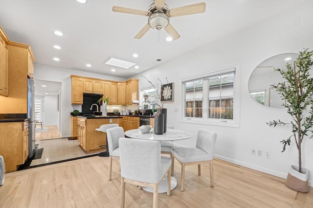 dining space featuring ceiling fan, light wood-type flooring, sink, and a skylight