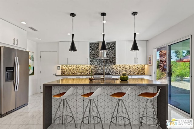 kitchen featuring decorative light fixtures, white cabinets, stainless steel fridge, and a kitchen breakfast bar