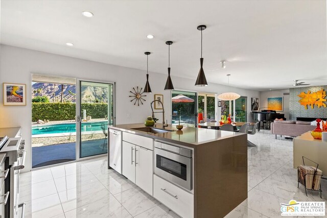 kitchen with stainless steel dishwasher, hanging light fixtures, a kitchen island with sink, white cabinetry, and sink