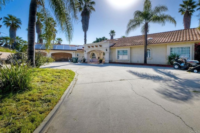 mediterranean / spanish-style home with driveway, a tiled roof, roof mounted solar panels, and stucco siding