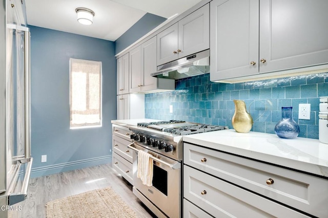 kitchen featuring light stone counters, stainless steel range, backsplash, and light wood-type flooring