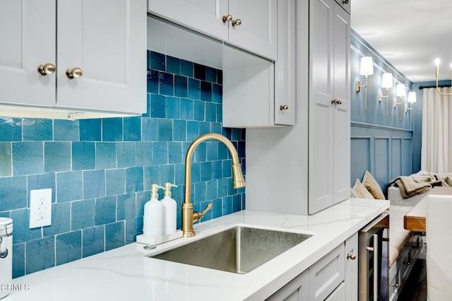 kitchen with white cabinetry, beverage cooler, light stone counters, and sink