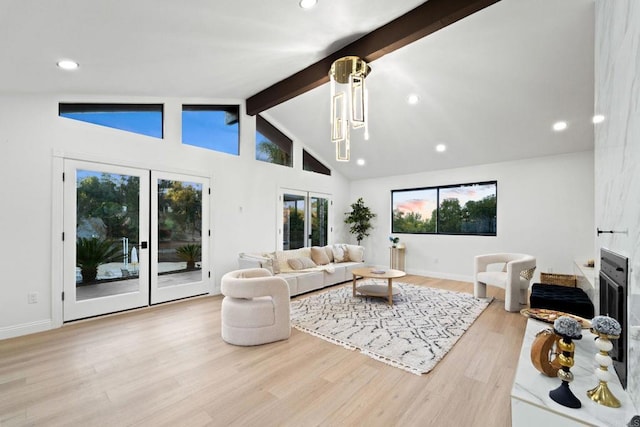 living room featuring vaulted ceiling with beams, a notable chandelier, a large fireplace, french doors, and light wood-type flooring