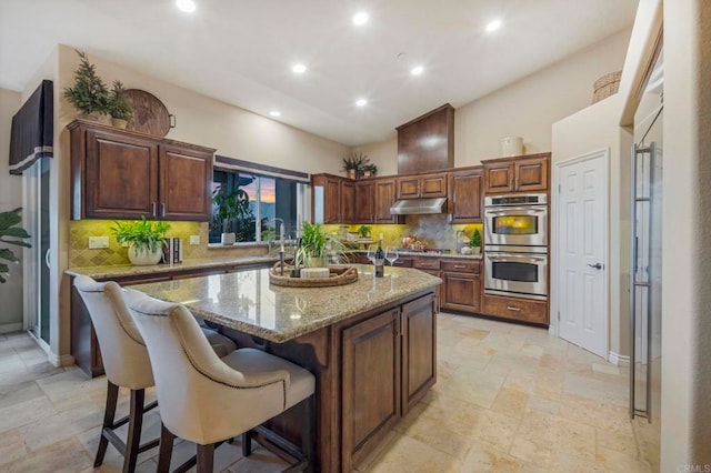 kitchen with light stone countertops, appliances with stainless steel finishes, a center island, backsplash, and a breakfast bar area