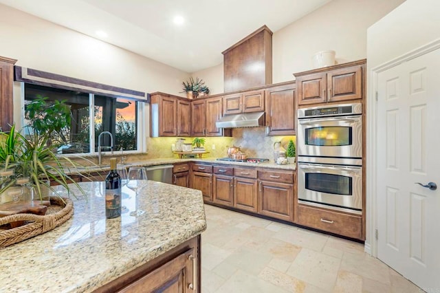 kitchen featuring stainless steel appliances, backsplash, light stone counters, and sink