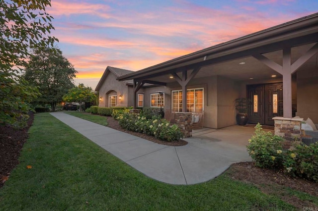 back house at dusk featuring a lawn