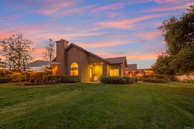 back house at dusk featuring a lawn