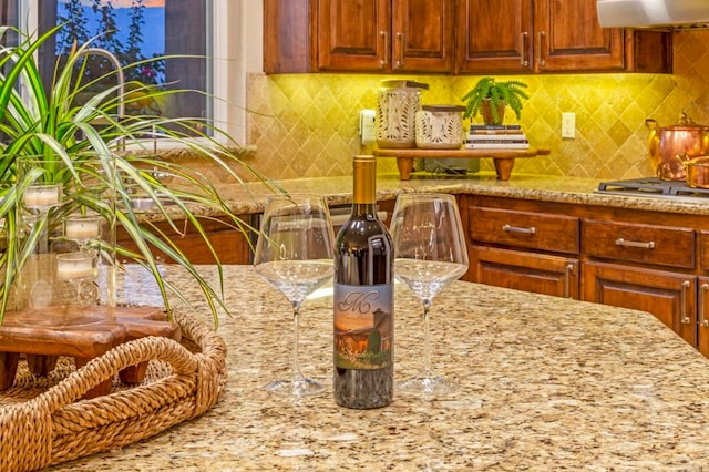 kitchen with exhaust hood, stainless steel gas cooktop, tasteful backsplash, and light stone countertops