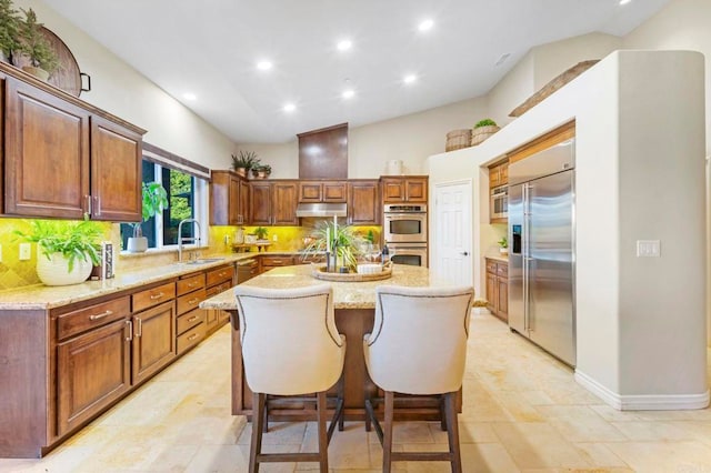 kitchen with backsplash, a kitchen island, sink, appliances with stainless steel finishes, and a breakfast bar area