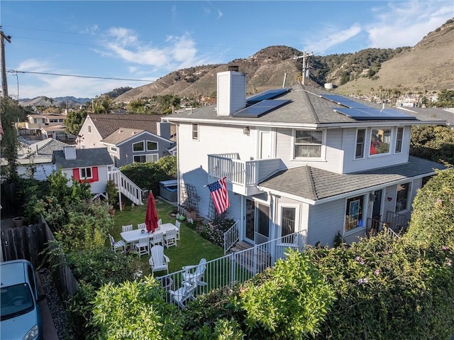 back of house with a mountain view, a balcony, solar panels, and a yard