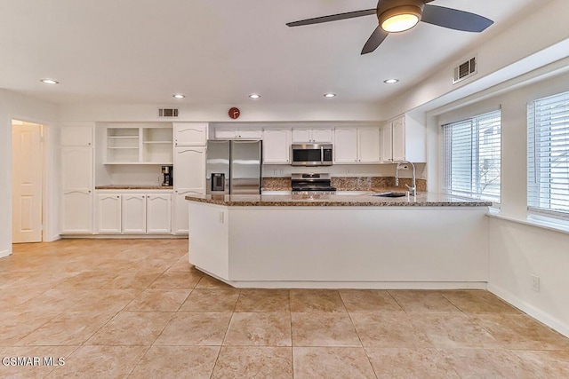 kitchen featuring dark stone countertops, kitchen peninsula, sink, appliances with stainless steel finishes, and white cabinets