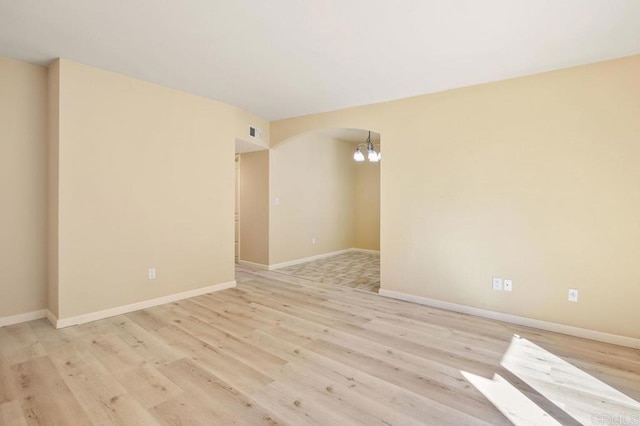 spare room with a notable chandelier and light hardwood / wood-style floors