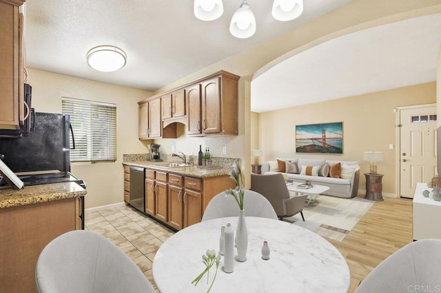 kitchen with black fridge, stainless steel dishwasher, sink, light wood-type flooring, and a textured ceiling