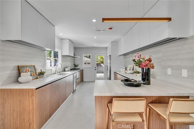 kitchen featuring white cabinetry, wall chimney range hood, tasteful backsplash, a kitchen breakfast bar, and sink