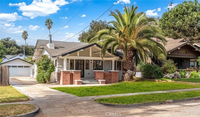 view of front of property featuring a front yard, covered porch, a garage, and an outbuilding