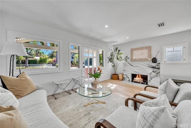 living room featuring light hardwood / wood-style flooring, a high end fireplace, and a healthy amount of sunlight