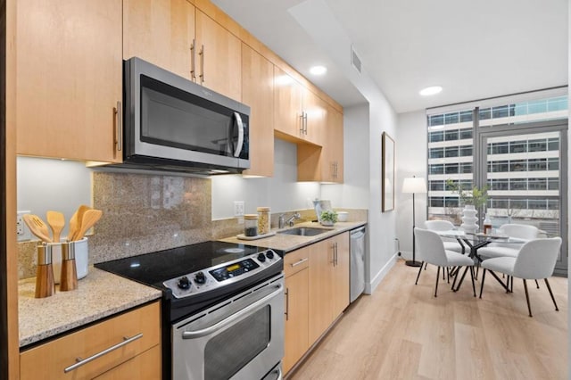 kitchen with stainless steel appliances, light brown cabinetry, light stone countertops, light hardwood / wood-style flooring, and sink