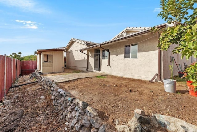 rear view of property with stucco siding, a fenced backyard, an outdoor structure, and a storage unit