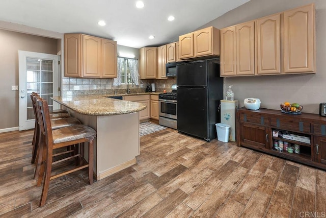 kitchen with light brown cabinets, black appliances, wood finished floors, and a sink