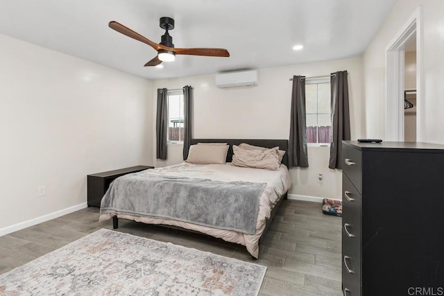 bedroom featuring wood finished floors, ceiling fan, baseboards, and a wall mounted AC