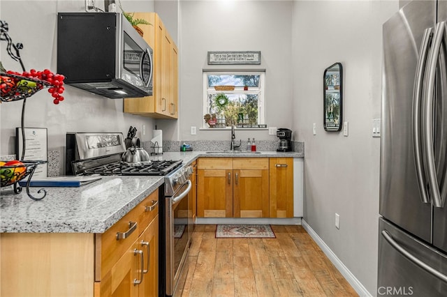 kitchen with stainless steel appliances, light hardwood / wood-style floors, sink, and light stone countertops