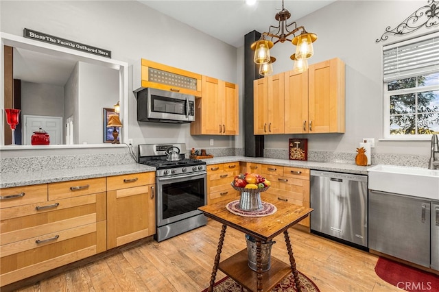 kitchen with an inviting chandelier, stainless steel appliances, sink, and light hardwood / wood-style flooring